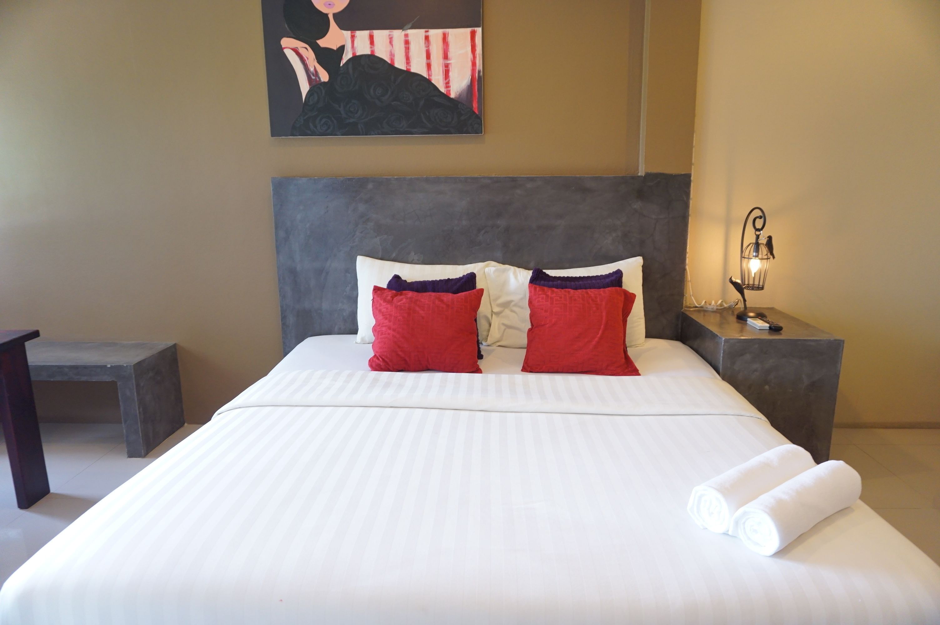 Una cama bien tendida con ropa de cama blanca y roja, un cabecero y una mesita de noche con una lámpara.