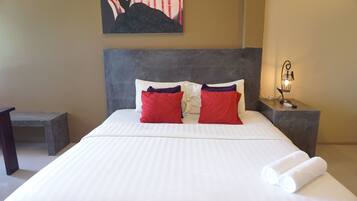 Una cama bien tendida con ropa de cama blanca y roja, un cabecero y una mesita de noche con una lámpara.
