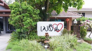 A sign with Thai characters and a heart symbol, surrounded by lush greenery and a traditional building in the background. - Ploenjai Hotel Ranong (Ranong)