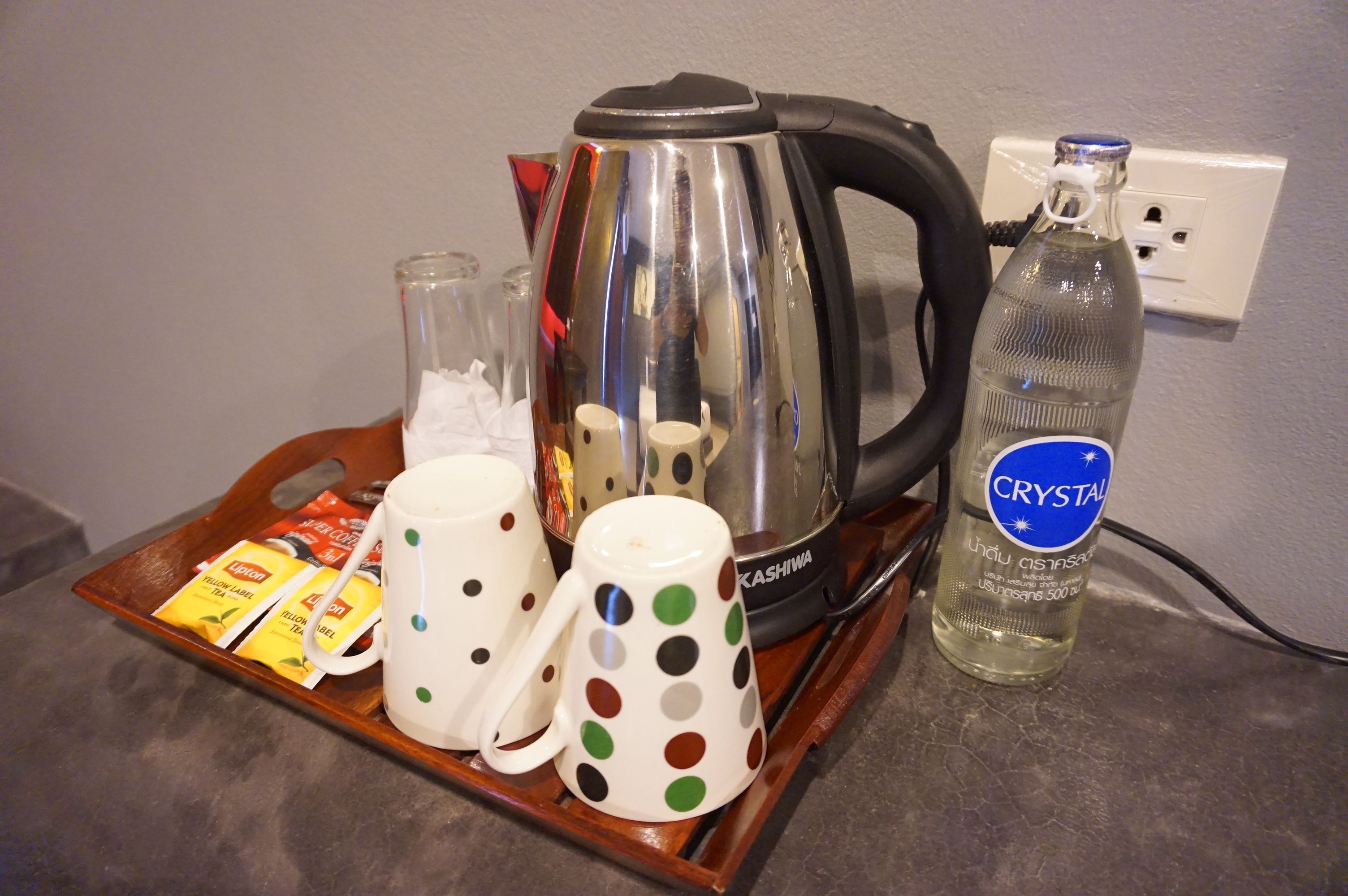 Una bandeja con un hervidor, dos tazas, un vaso y una botella de agua Crystal sobre una encimera.