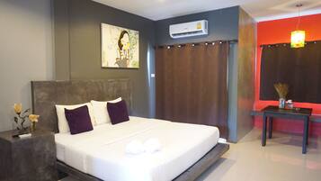 A modern hotel room with a large bed, a nightstand, an air conditioning unit, a small table with a vase, and a painting on the wall.