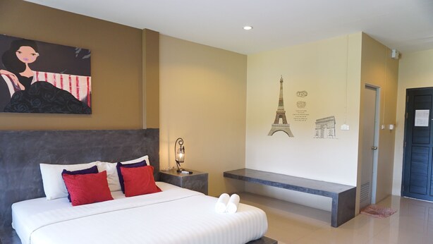 A modern hotel room with a large bed, a nightstand, a bench, and a wall with a painting and a depiction of the Eiffel Tower. - Ploenjai Hotel Ranong (Ranong)