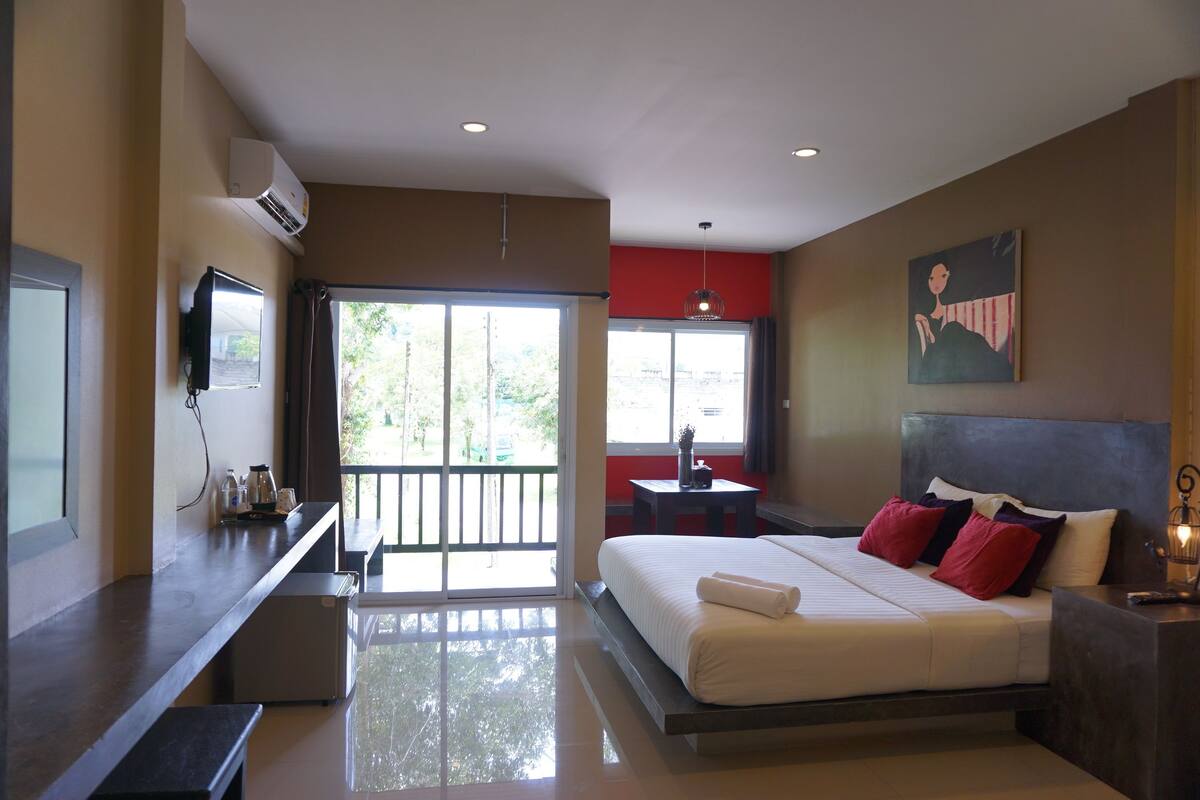 A modern hotel room with a large bed, a TV, a desk, and a balcony with a view.