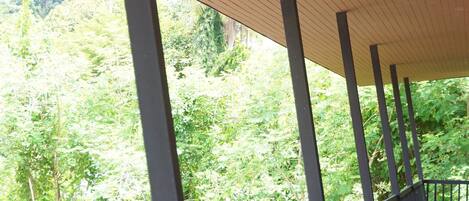 Un espacio al aire libre techado, con techo de madera y barandillas metálicas, que da a un exuberante paisaje verde.