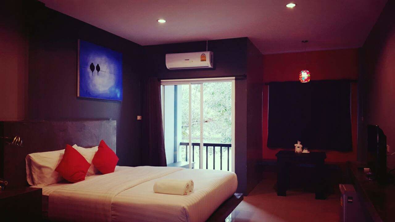 Une chambre à coucher avec un lit, des oreillers rouges, une fenêtre, un appareil de climatisation et un téléviseur.