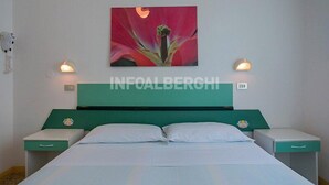 A hotel room with a teal headboard, two bedside tables, white bedding, and a wall-mounted artwork of a flower. - Hotel Villa Pozzi (Cattolica)