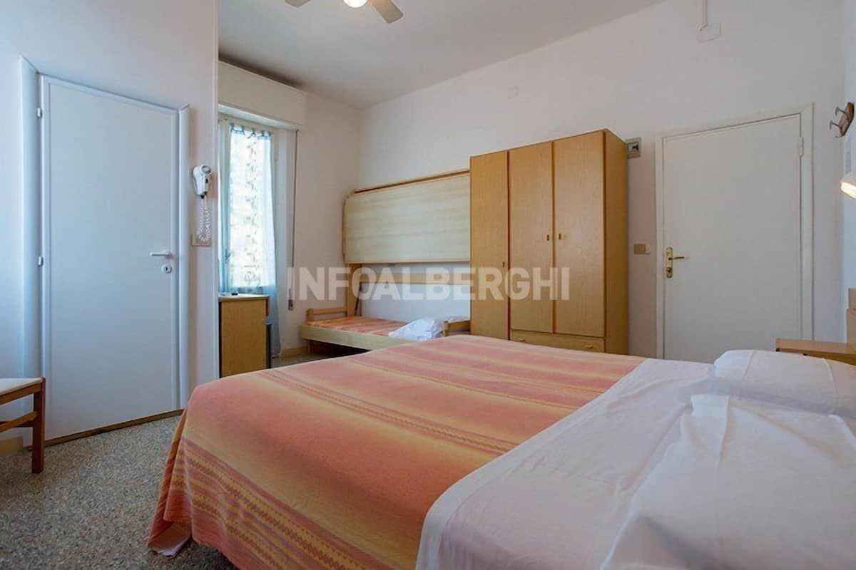 Quarto com duas camas, um guarda-roupa, uma escrivaninha e uma cadeira.