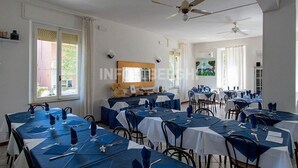 A spacious dining area with multiple tables set for dining, ceiling fans, and large windows allowing natural light. - Hotel Villa Pozzi (Cattolica)