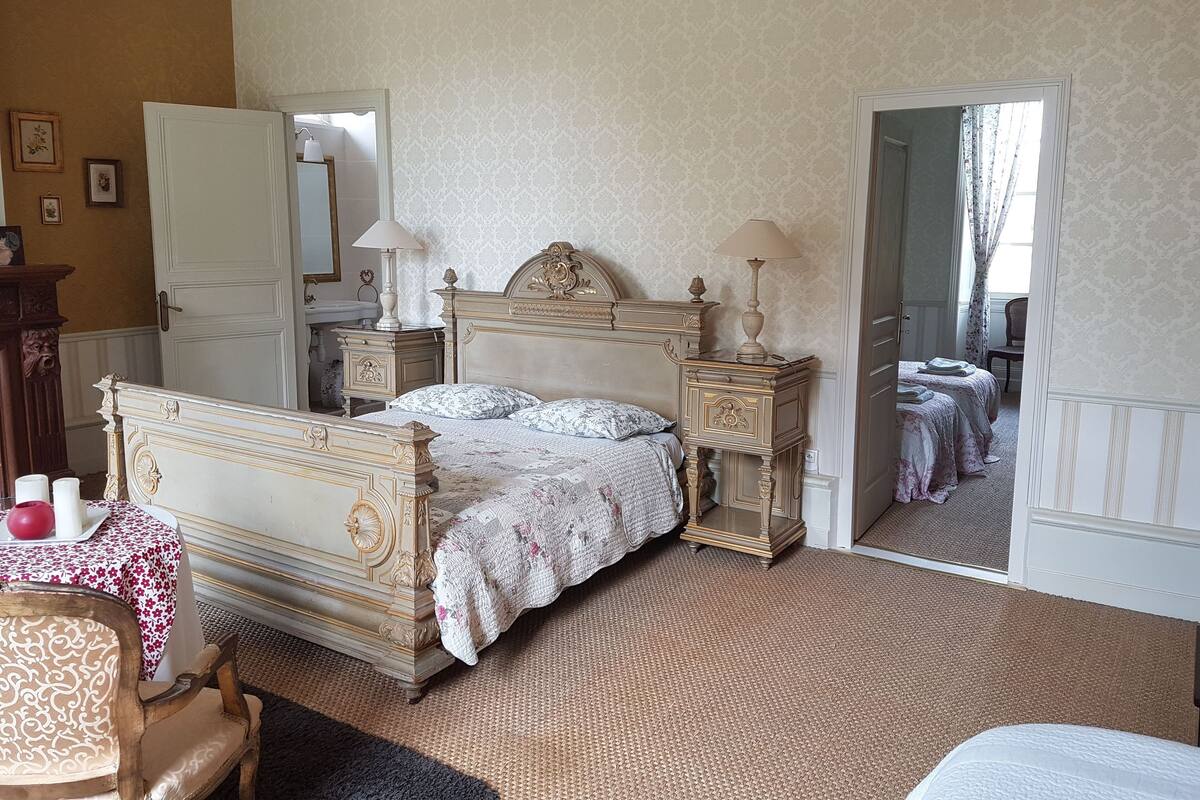 A classic bedroom with a large bed, two bedside tables, a nightstand, a dresser, a mirror, and a chair.