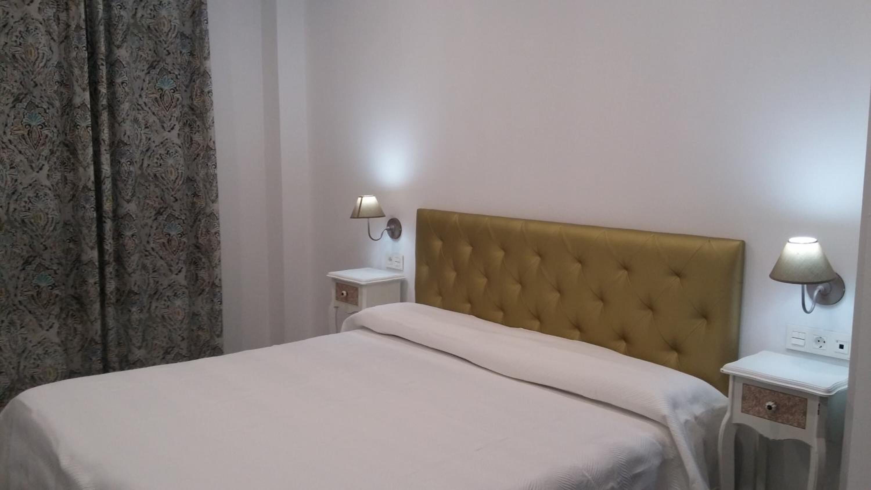 Una camera d'albergo con un letto, due comodini e una lampada a parete.