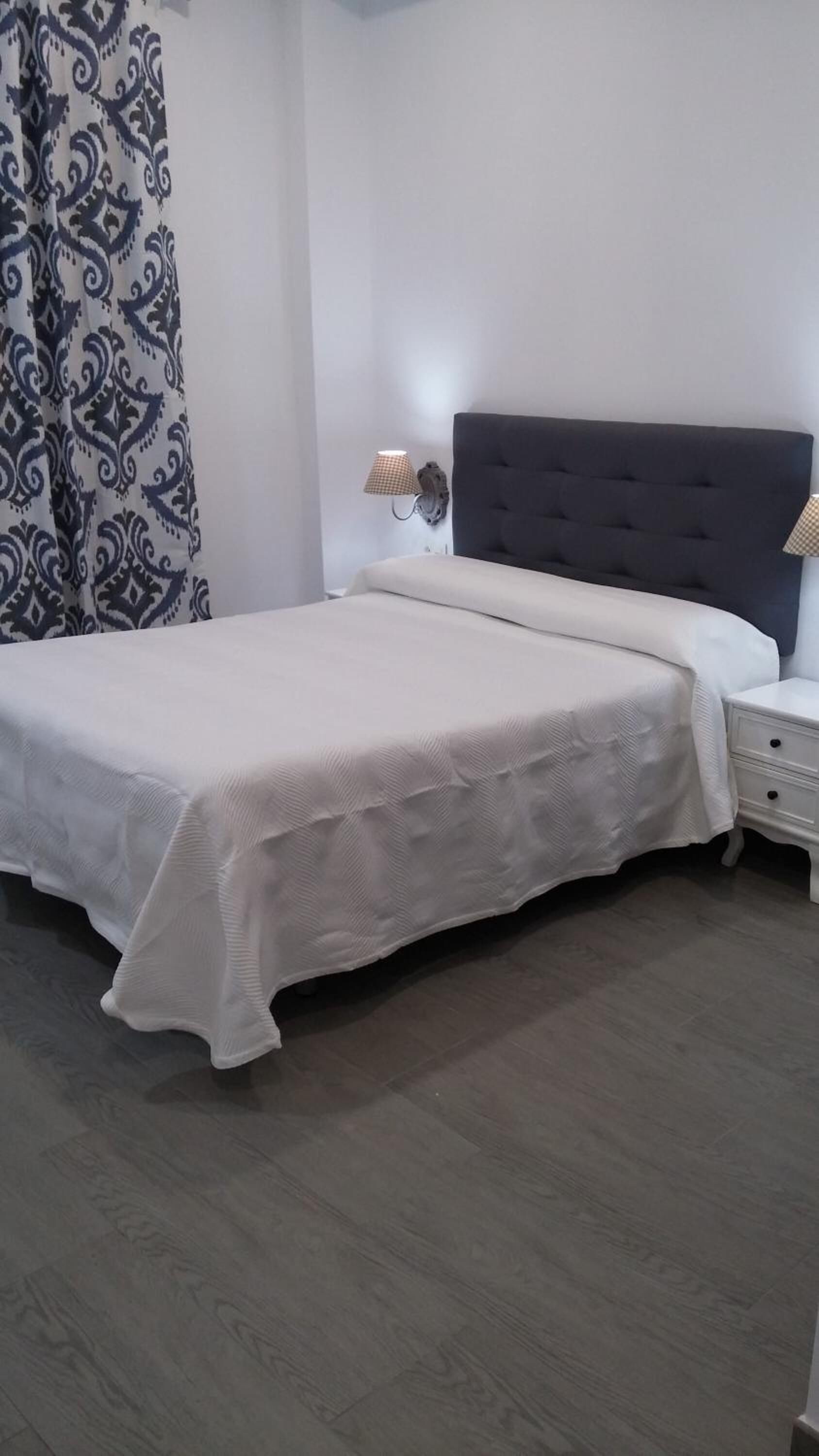 Een slaapkamer met een bed, nachtkastjes en een gordijn met dessin.