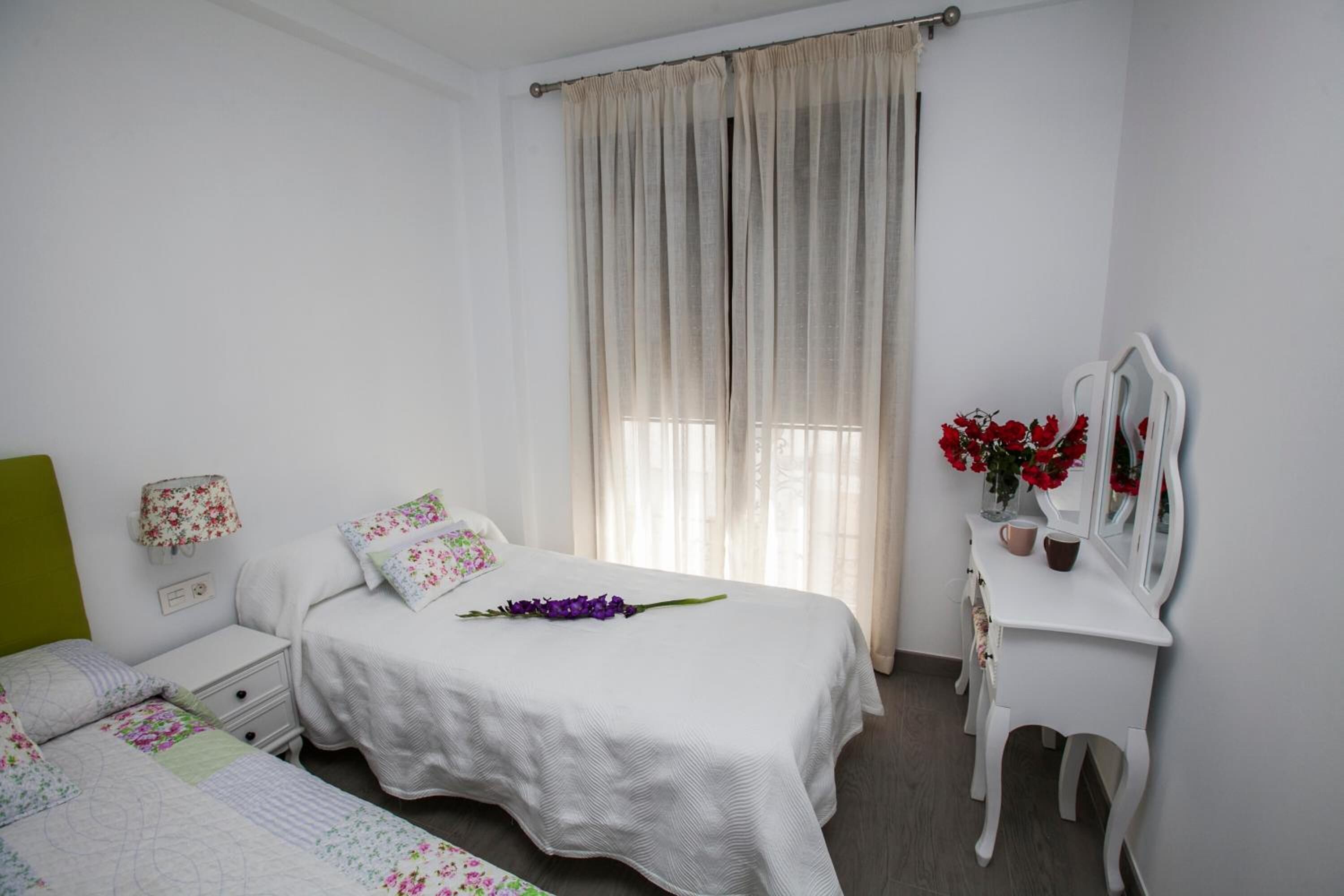Une chambre à coucher avec un lit, une table de chevet, une commode et une fenêtre avec des rideaux.