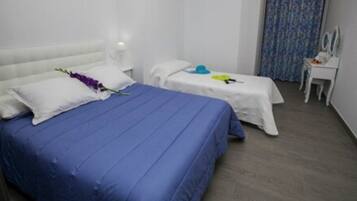 Une chambre d’hôtel avec deux lits, chacun doté d’une tête de lit blanche et d’une couvre-lit bleue. Une petite table avec un miroir et une lampe se trouve sur le côté droit.