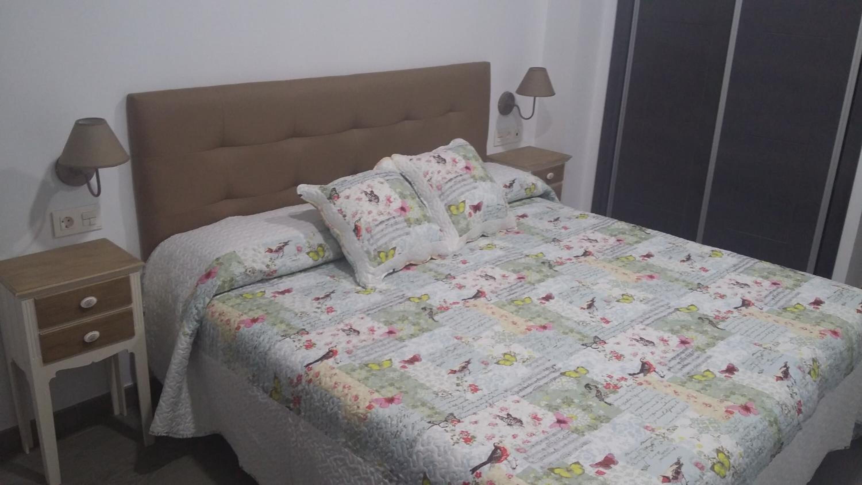 A bedroom with a bed, two nightstands, a wardrobe, and a wall-mounted lamp.