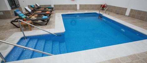 An indoor swimming pool with steps leading into the water, lounge chairs, and a lifebuoy on the wall.