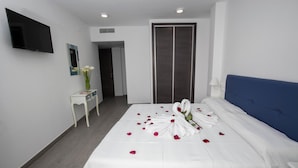 A hotel room with a bed, a TV mounted on the wall, a small table with a vase of flowers, and a door. - Hostal Boutique Bajamar (Nerja)