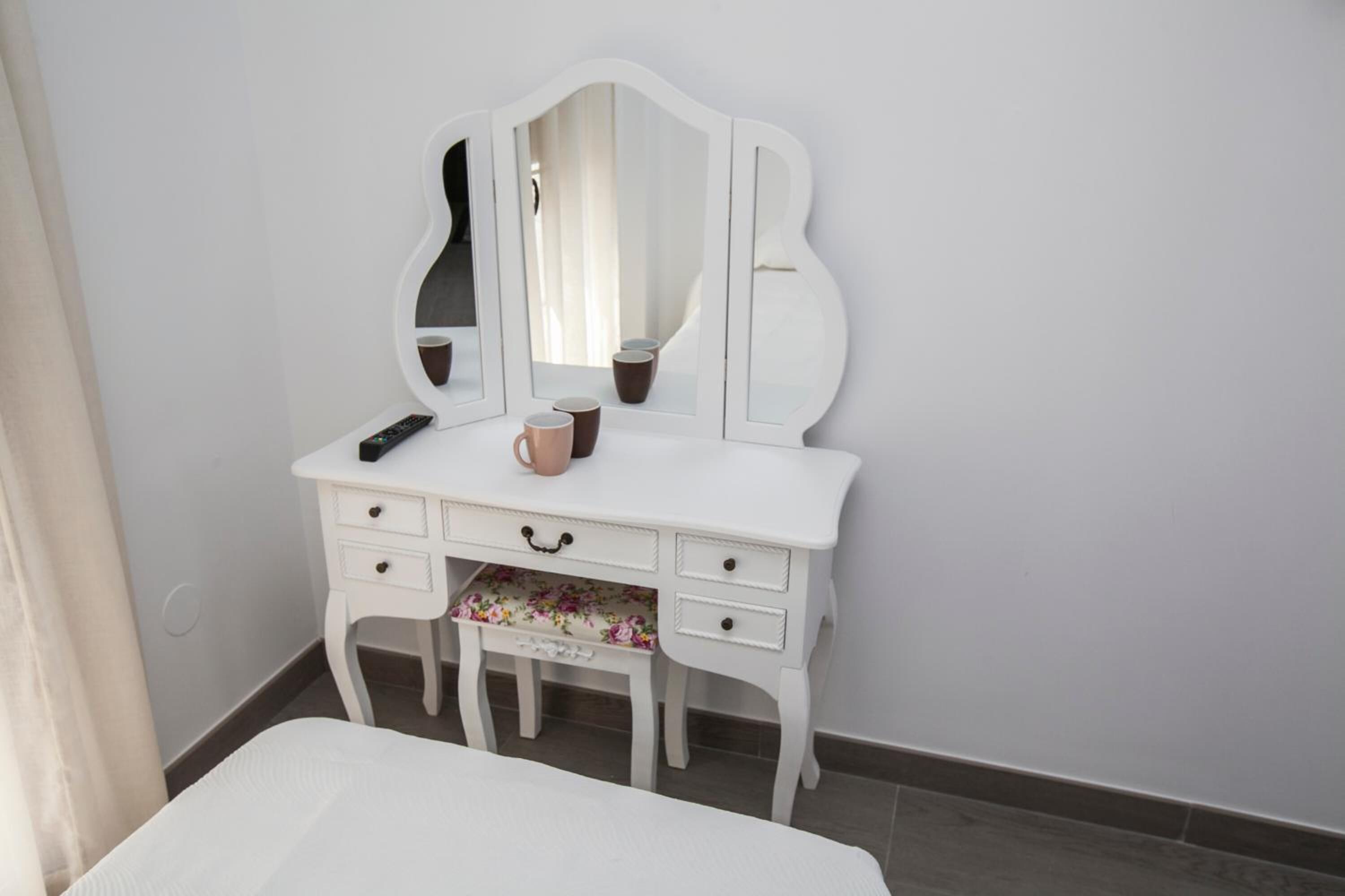 A white vanity with a mirror, a remote control, and a mug on it.
