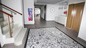 A modern hallway with a patterned rug, a staircase, a wall clock, and a bench. - Hostal Boutique Bajamar (Nerja)