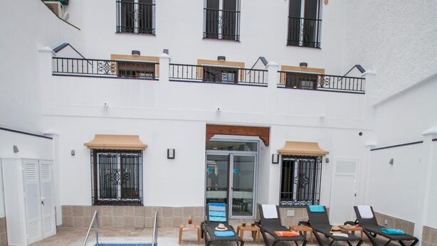 A swimming pool with lounge chairs and a building with balconies. - Hostal Boutique Bajamar (Nerja)
