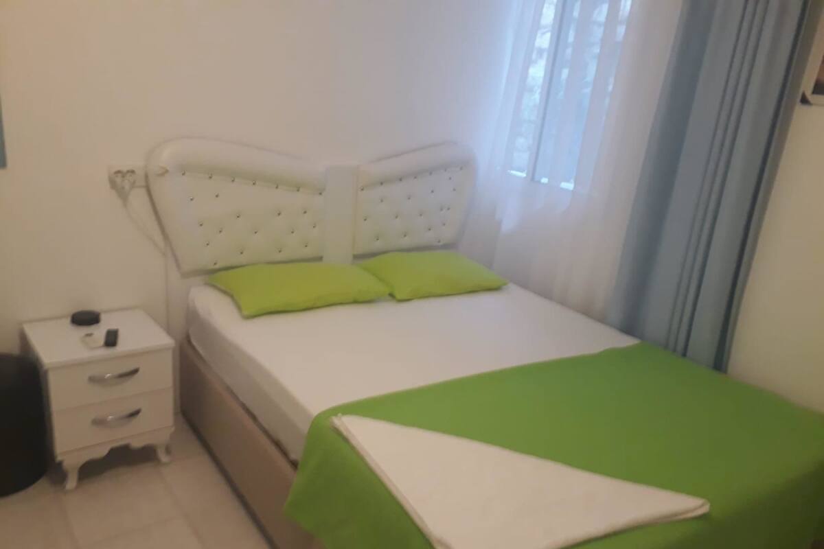 A bedroom with a bed, a nightstand, and a window with curtains.
