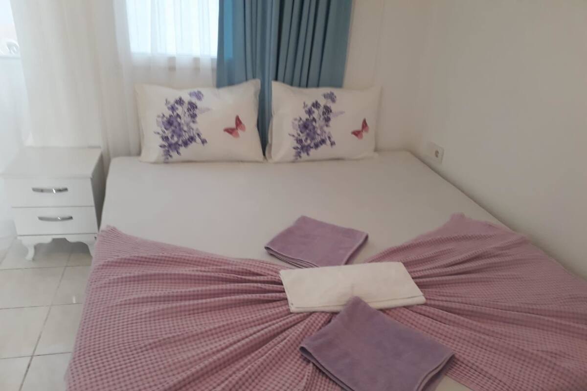 A neatly made bed with a pink checkered bedspread and two folded purple towels.