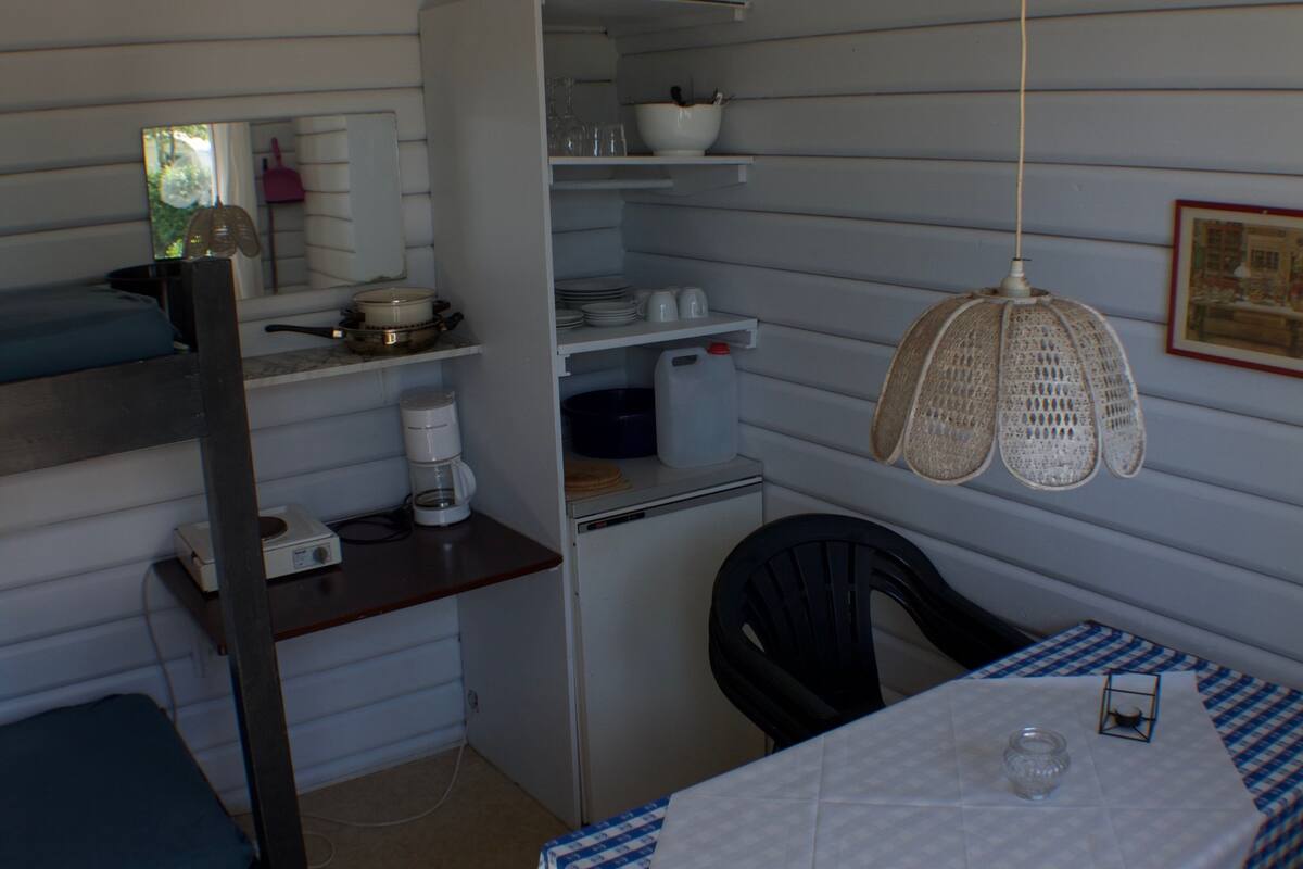 Una habitación compacta con literas, una kitchenette pequeña, una mesa de comedor con mantel a cuadros y una lámpara colgante.