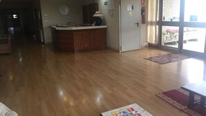 Tilava aula, jossa on puinen vastaanottotiski, kello ja palosammutin.