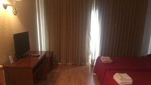 Hotellihuone, jossa on puinen työpöytä, televisio, punaisella päällisellä varustettu sänky ja ikkuna, jossa on verhot.