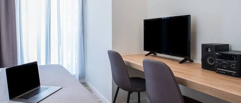 Quarto de hotel moderno com uma cama, uma escrivaninha com um laptop, uma televisão e um sistema de som.