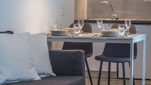 A modern dining area with a white table set for four, two grey chairs, and a grey sofa with a white pillow. - Spot Apart (Athens)