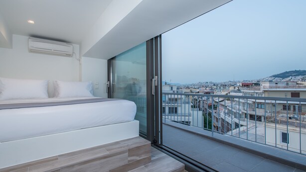 A modern bedroom with a large bed, a glass door leading to a balcony with a city view. - Spot Apart (Athens)