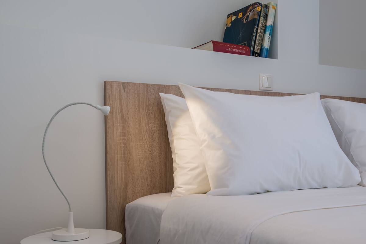 A neatly made bed with white bedding, a wooden headboard, and a bedside lamp.
