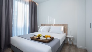 A hotel room with a bed, a bedside table, a lamp, and a breakfast tray with fruits and drinks. - Spot Apart (Athens)