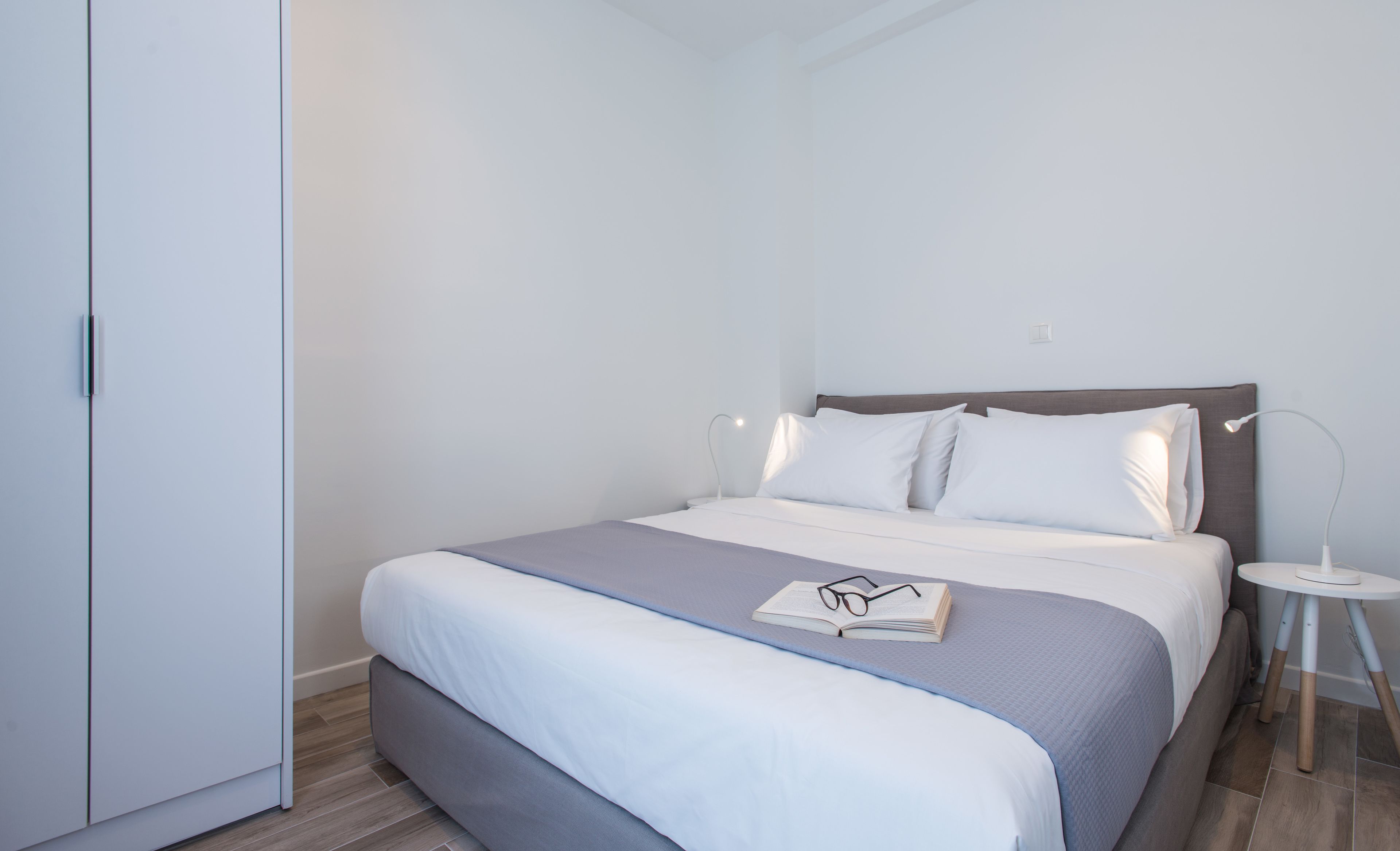 A neatly made bed with a grey and white duvet, a bedside table with a lamp, and a wardrobe.