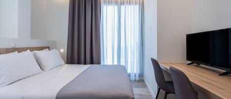 A hotel room with a bed, a desk, a television, and a window with curtains.