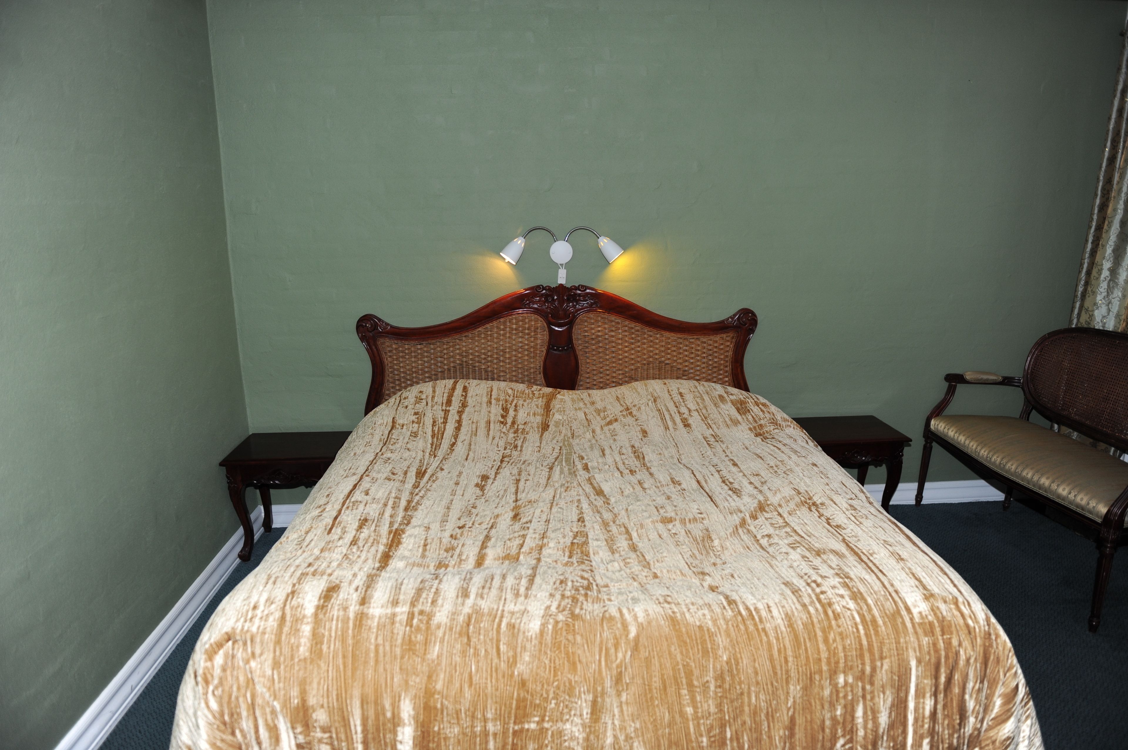 A bed with a headboard, two bedside tables, a chair, and a wall-mounted lamp.