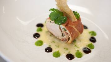 A white plate with a piece of meat, green leaves, and dark sauce.