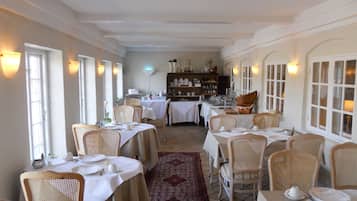 Un espace repas avec des tables dressées pour le service, des chaises en osier et un buffet en arrière-plan.