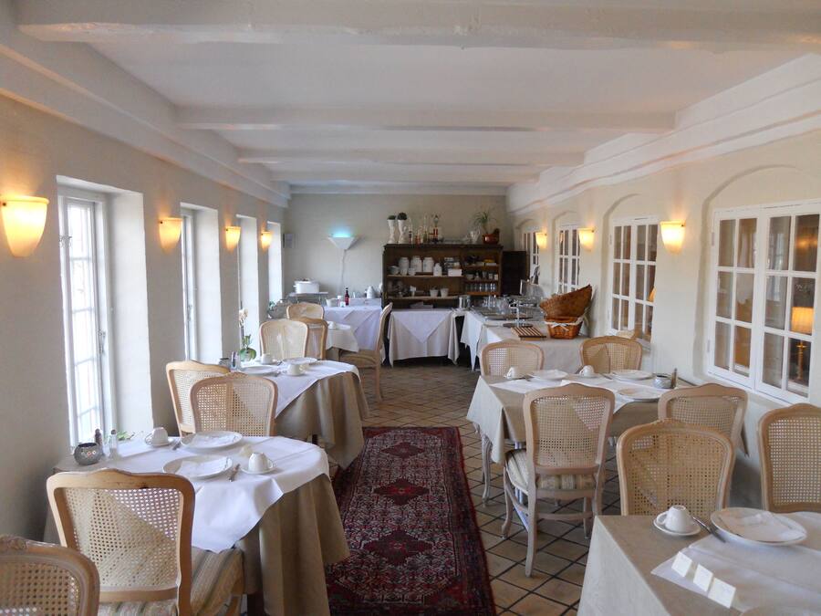 Un espace repas avec des tables dressées pour le service, des chaises en osier et un buffet en arrière-plan.