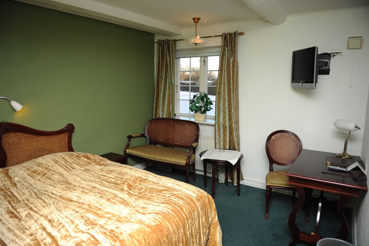 A hotel room with a bed, two chairs, a small table, a television, and a window with curtains.