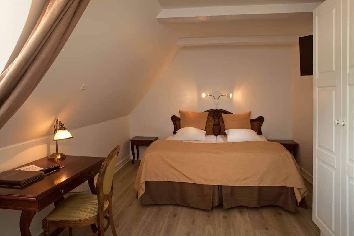 A bedroom with a bed, bedside tables, a desk, a chair, and a lamp.