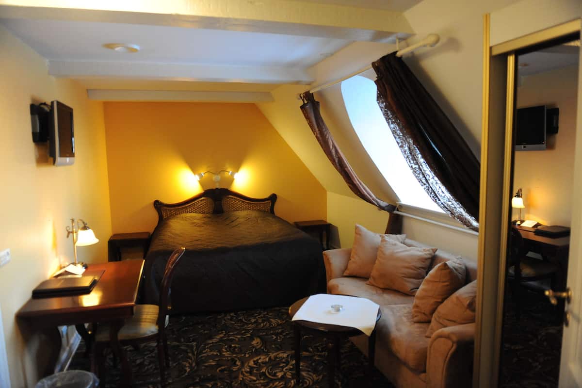 A hotel room with a bed, a desk, a chair, a sofa, a TV, and a window with curtains.