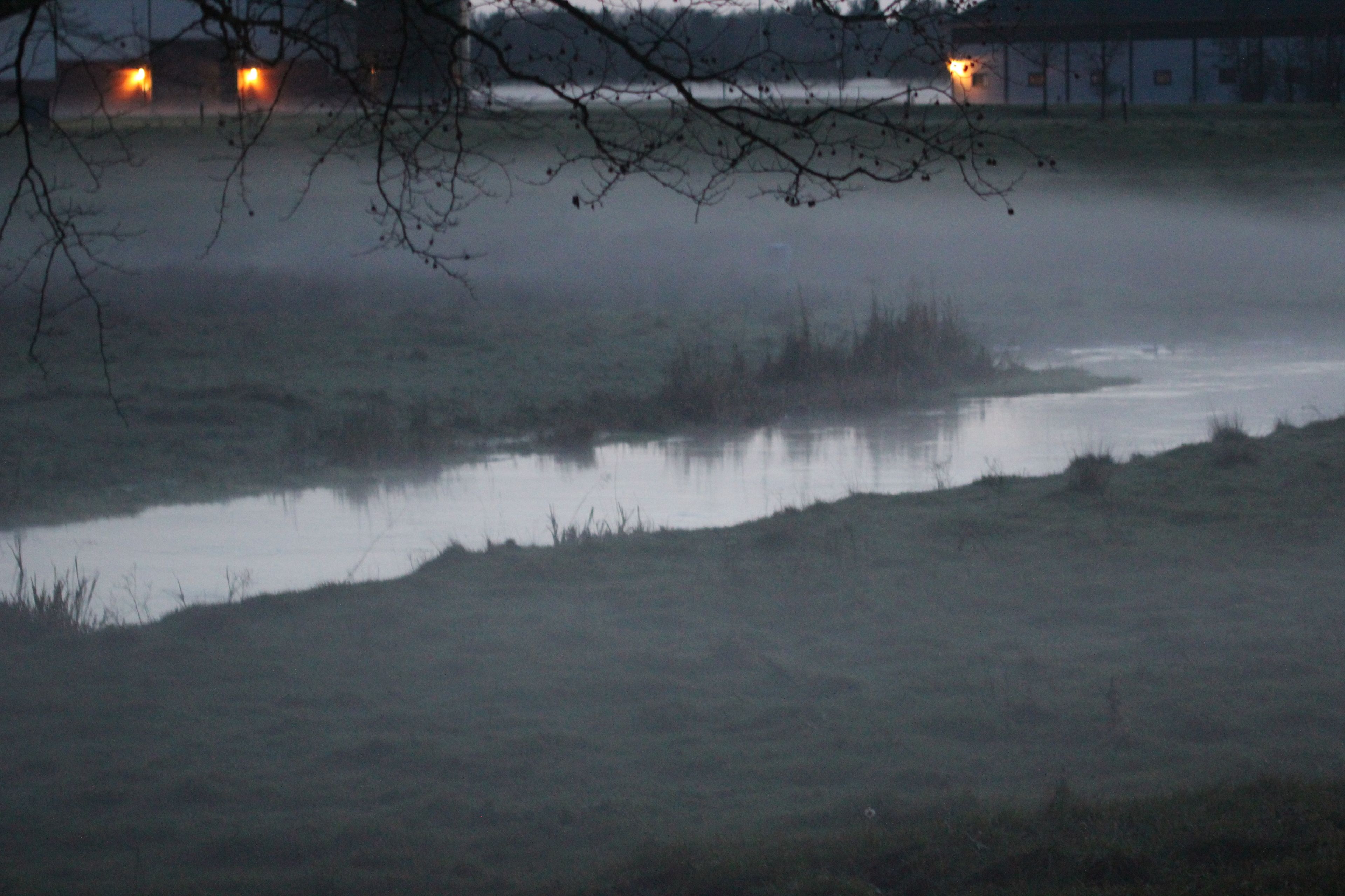 A foggy landscape with a body of water and distant lights.