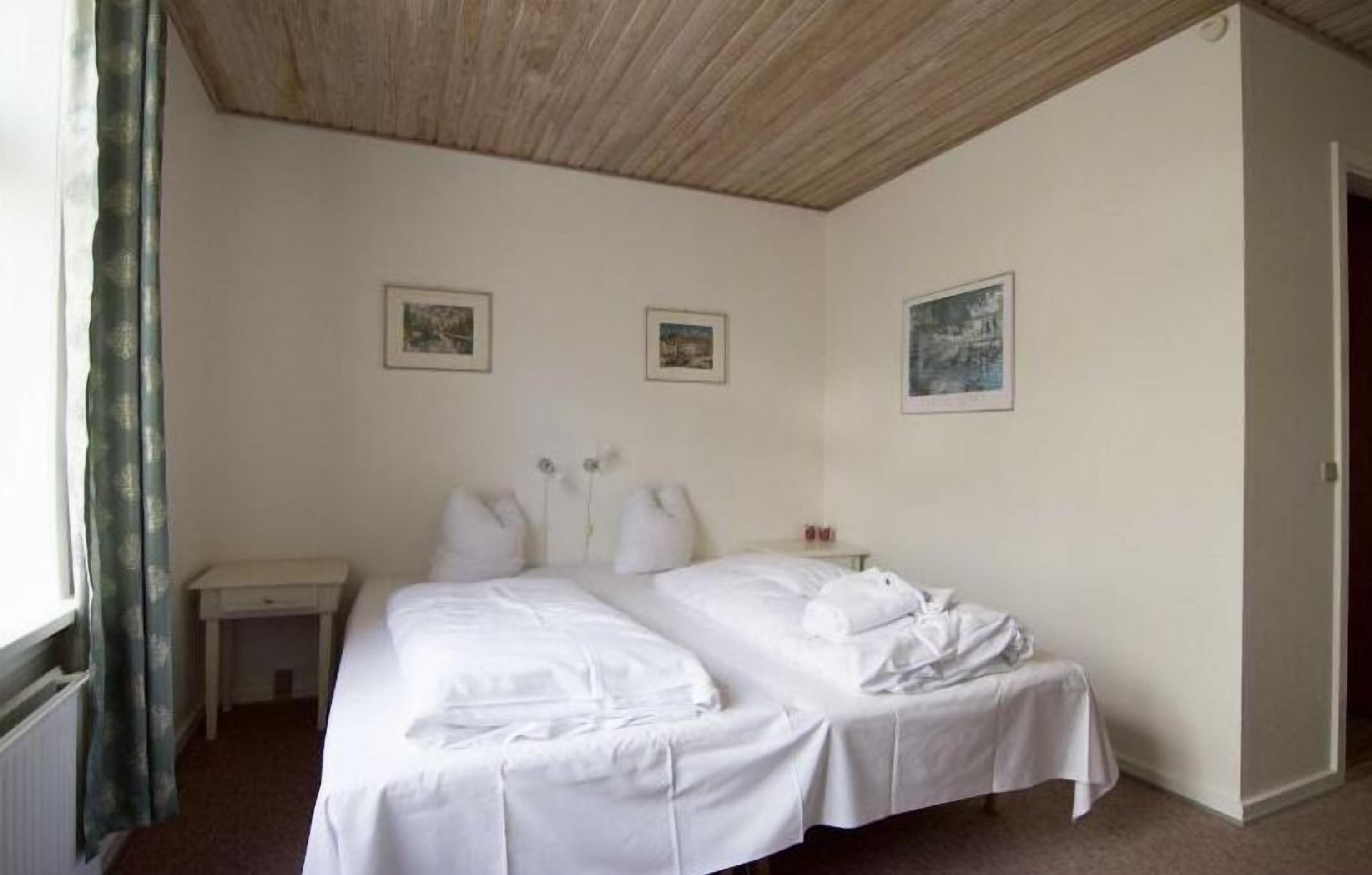 Una cama doble con sábanas blancas, una mesita de noche y una lámpara.
