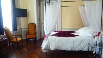A bedroom with a four-poster bed, a chair, a bedside table, and a TV mounted on the wall.