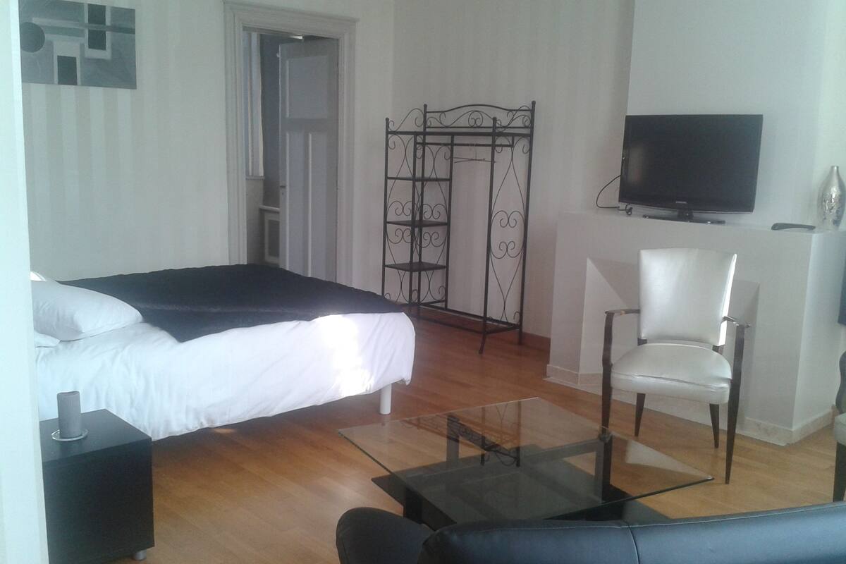 Quarto com uma cama, televisão, cadeira e uma pequena mesa.