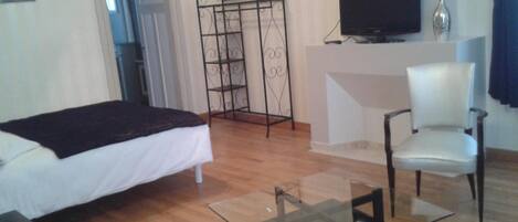 A hotel room with a bed, a TV, a chair, and a glass table.