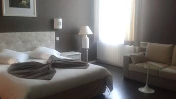 Une chambre d’hôtel avec un grand lit, une table de chevet, une lampe, un canapé et une fenêtre avec des rideaux.
