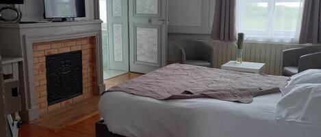 Un dormitorio con cama, televisión sobre una repisa, chimenea y ventana con cortinas.