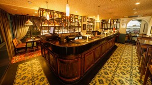 A bar area with a wooden counter, shelves with bottles, and a patterned carpet. - Woodapple Residency (New Delhi)